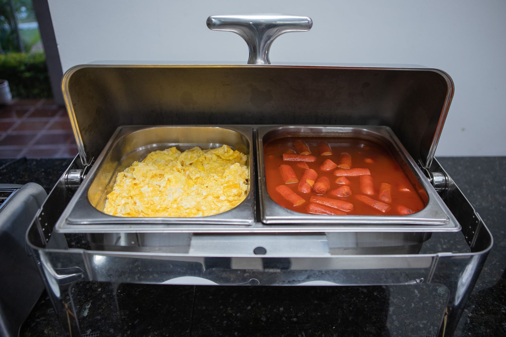 Aquecedor de buffet em aço inoxidável com ovos mexidos e linguiça ao molho.