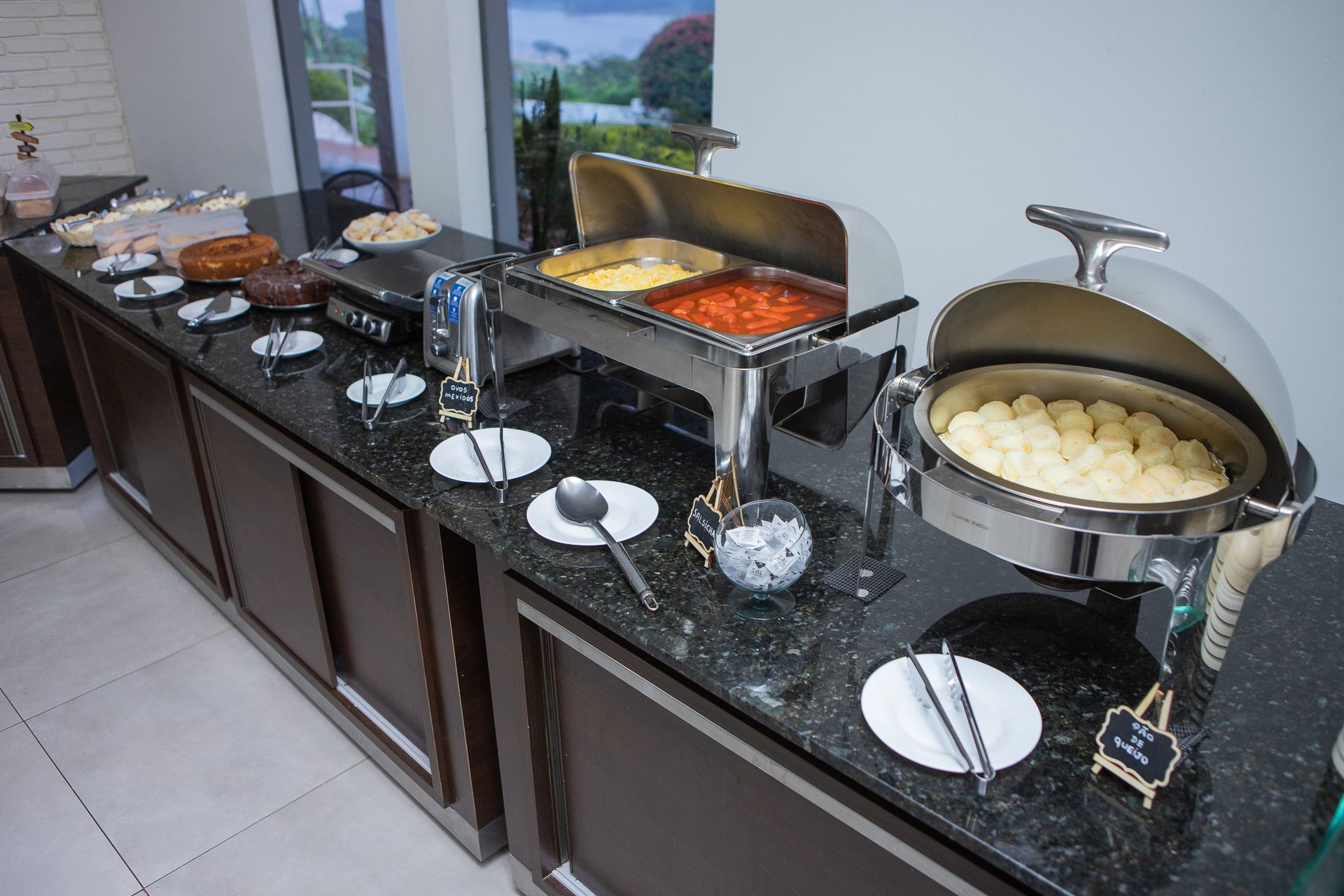 Buffet com diversos itens alimentícios em uma bancada, incluindo ovos mexidos, tomates e batatas.