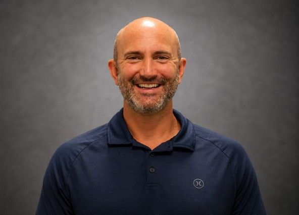Smiling bald man in a navy polo shirt against a gray studio background