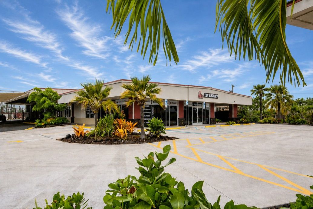 Sunny exterior of a small storefront with palm trees and an empty parking lot