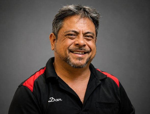 Smiling man in a black polo with red肩 panels against a gray studio background