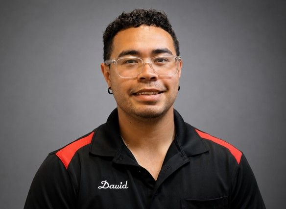 Portrait of a man in a black shirt with red shoulder accents, smiling against a gray background