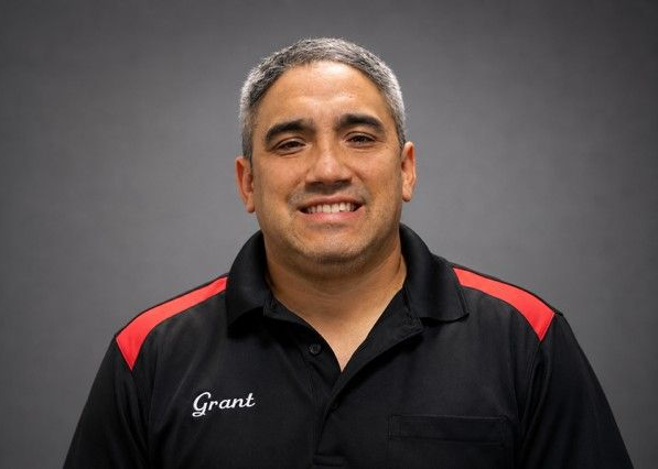 Smiling man in black polo with red accents against a gray background