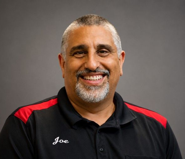 Smiling man in a black polo with red shoulder accents, against a gray background.