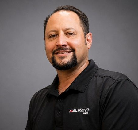 Portrait of a smiling man in a black polo shirt against a gray background