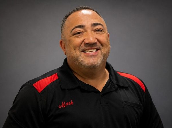Smiling man in a black polo with red shoulder accents against a gray background