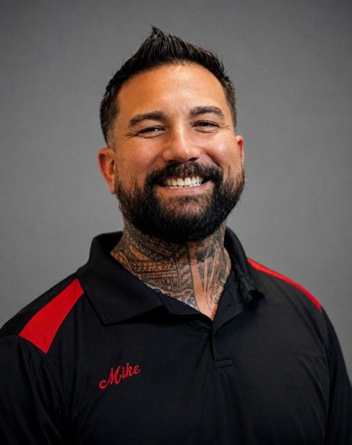 Smiling man in black polo with red shoulder accents and neck tattoo against a gray background