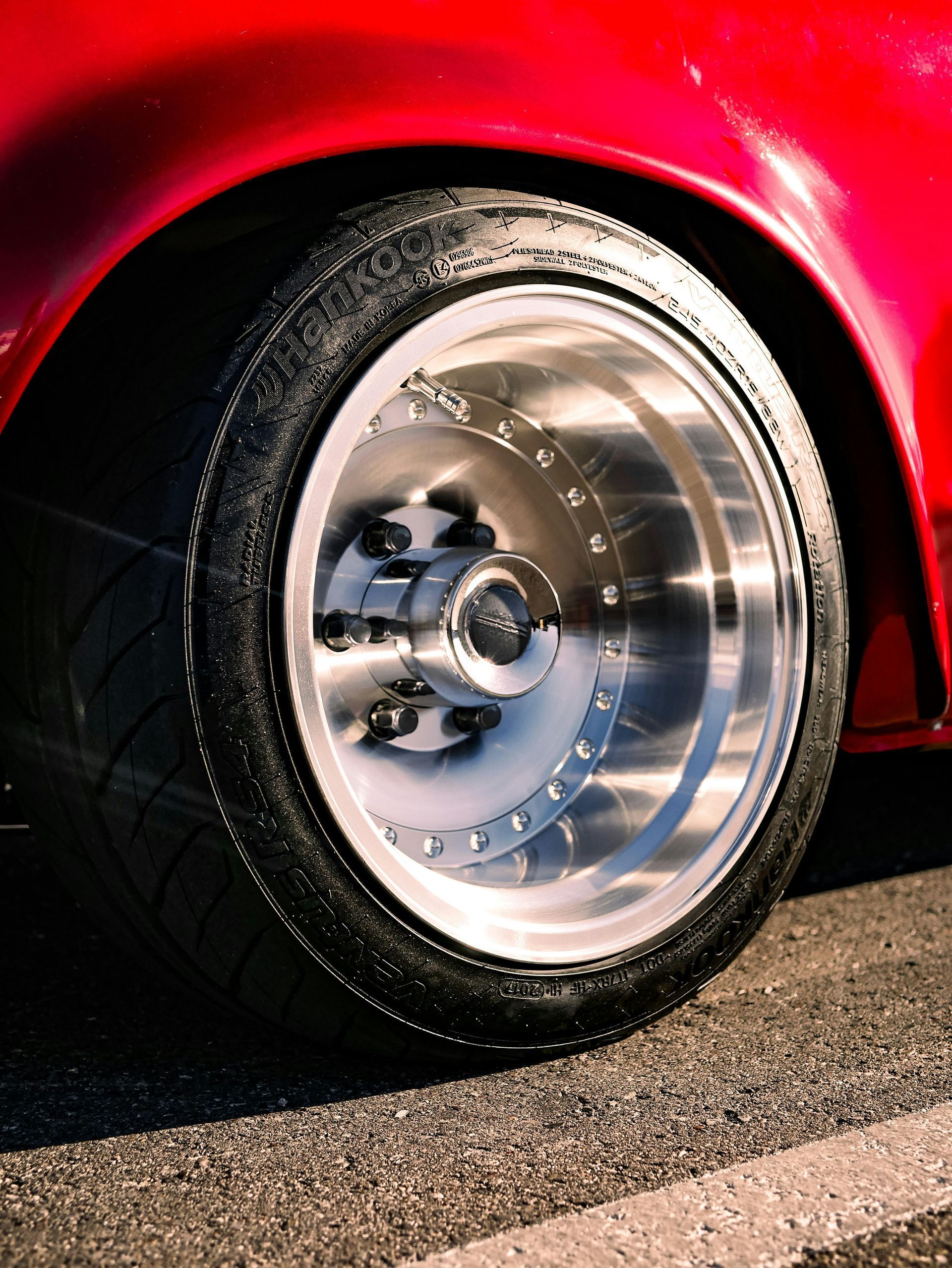Close-up of a car's red fender and a shiny silver wheel with a black tire on asphalt.
