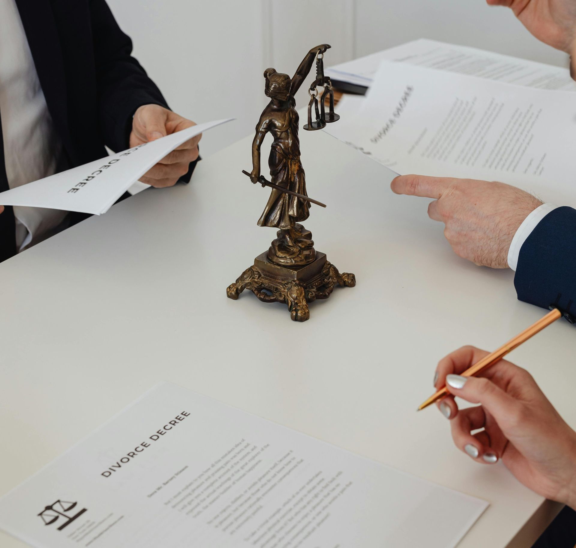 Two people are sitting at a table with papers and a statue of lady justice