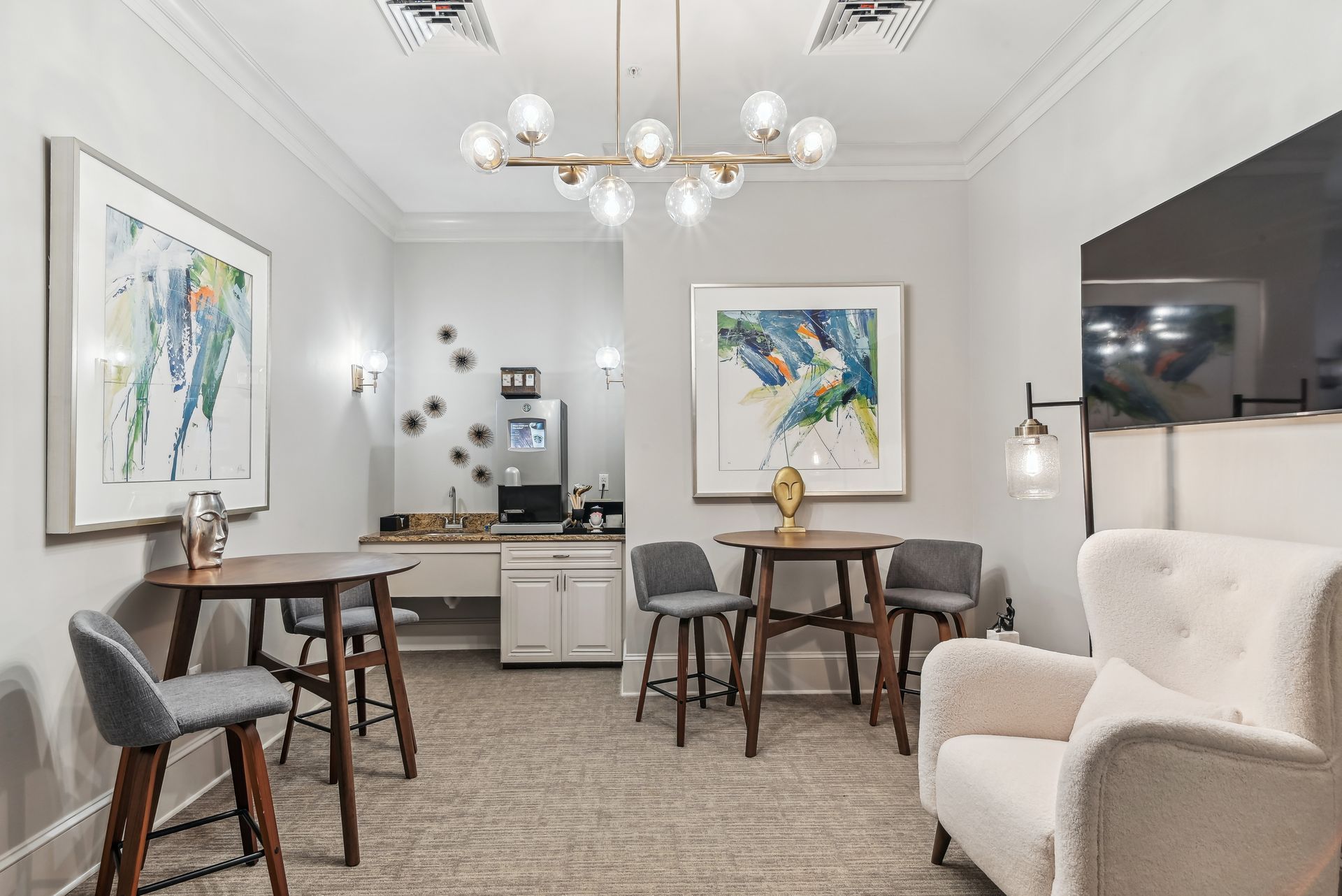 Cozy lounge area with bar tables, chairs, art, a sofa, and a light fixture.