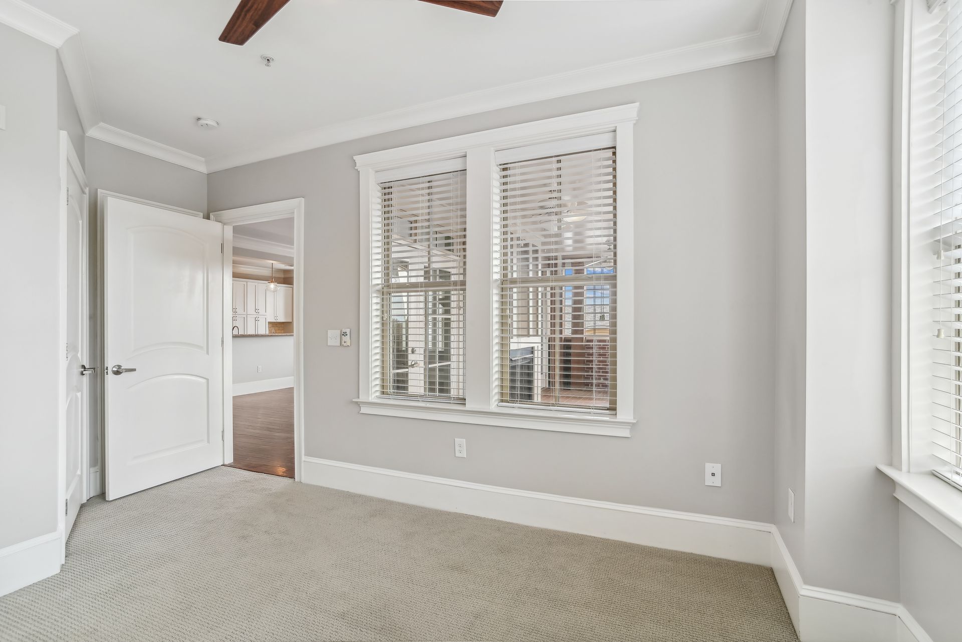 Empty room with gray walls, window with blinds, open door, and carpeted floor.
