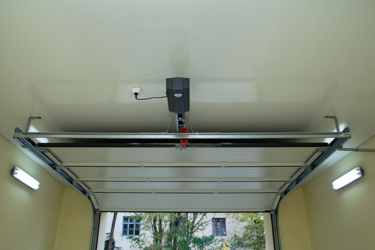 Garage interior with automated opener, open door, and lights.