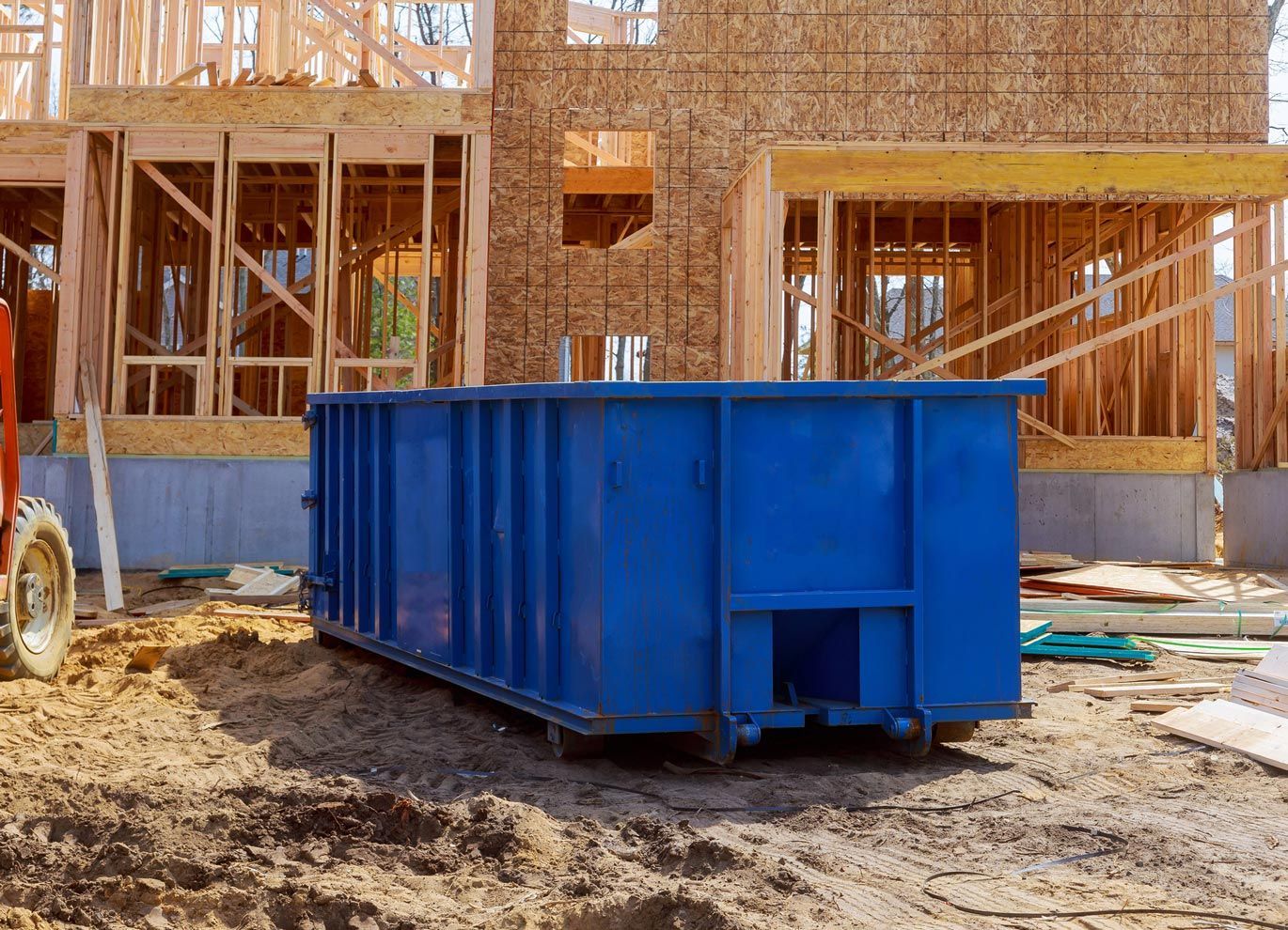 A blue dumpster is parked in front of a house under construction.