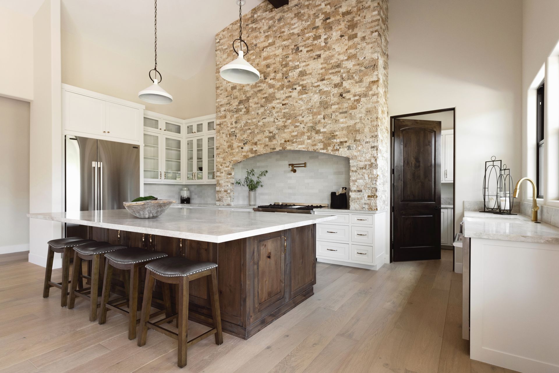 Modern kitchen with stone accent wall, dark wood island, white cabinets, and pendant lights