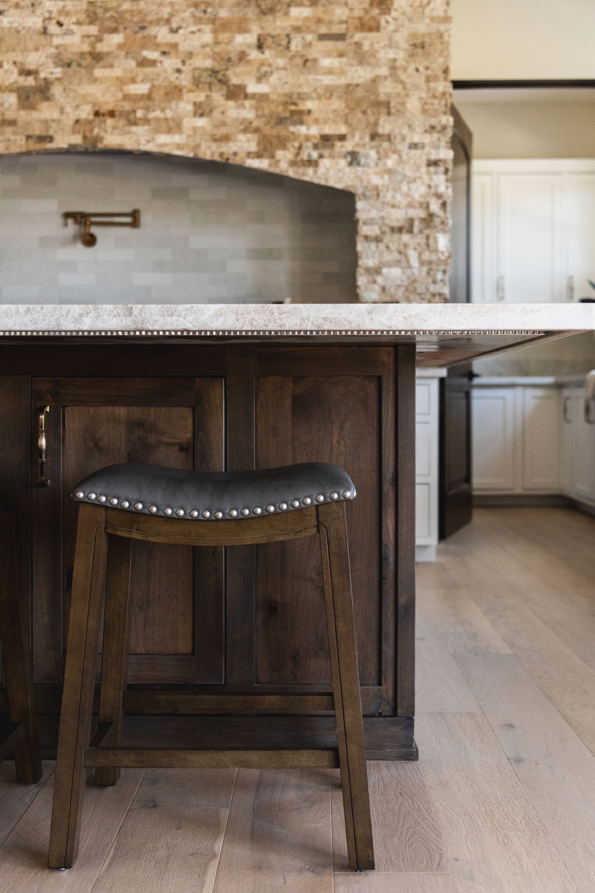 Rustic kitchen with stone wall, wooden island, and backless stool beneath a countertop.