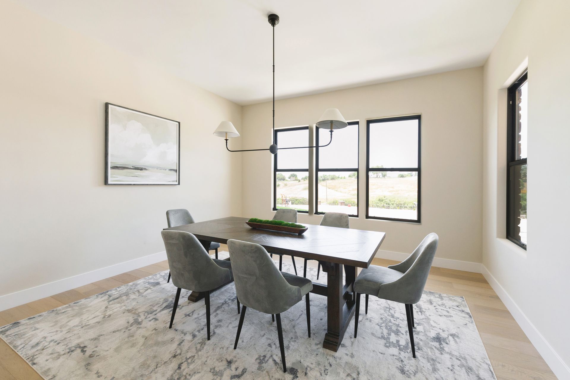 Modern dining room with a wooden table, gray chairs, large windows, and a patterned rug.