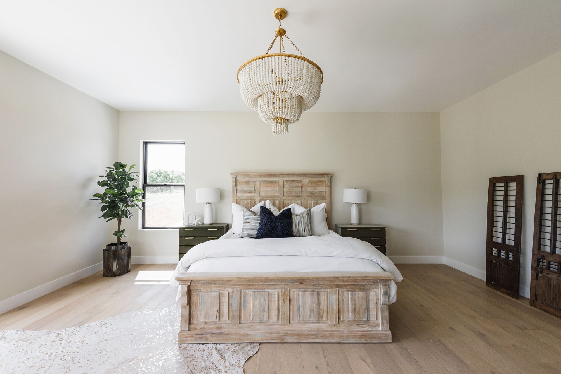 Bright bedroom with a wooden bed, chandelier, large window, and light neutral decor.