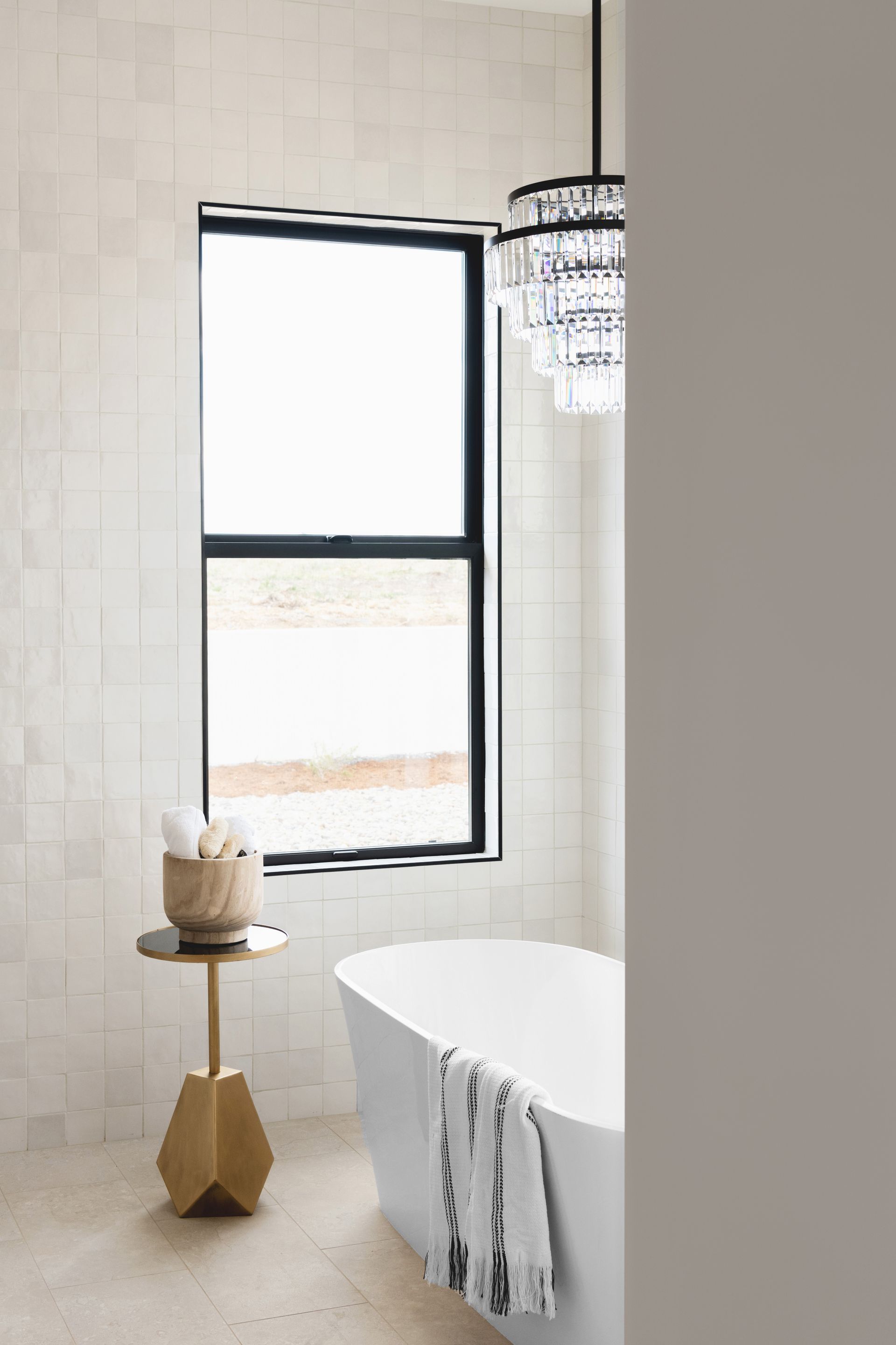 Bright bathroom with a white freestanding tub, black-framed window, and small side table.