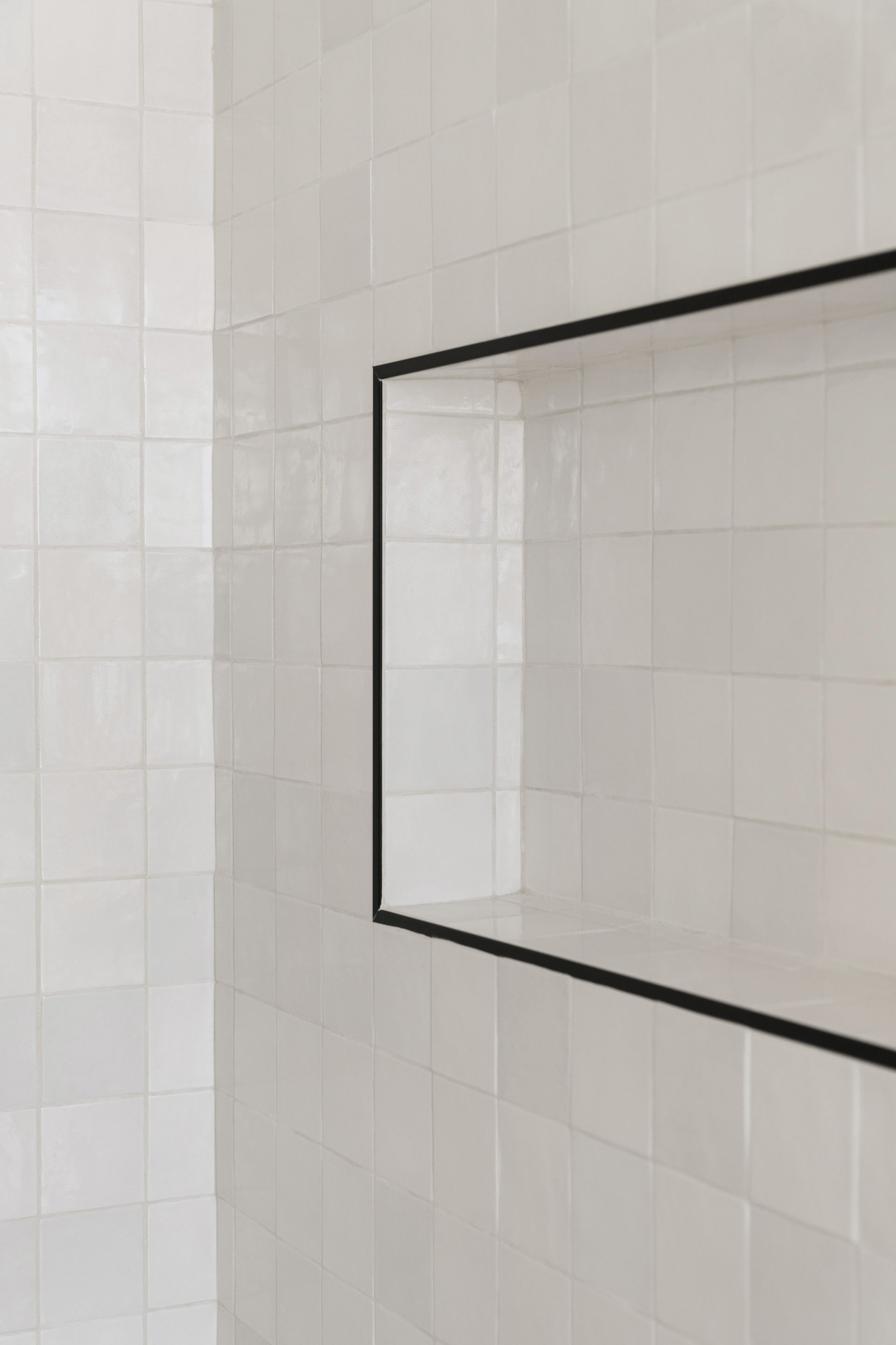 White tiled bathroom wall with a black-framed mirror.