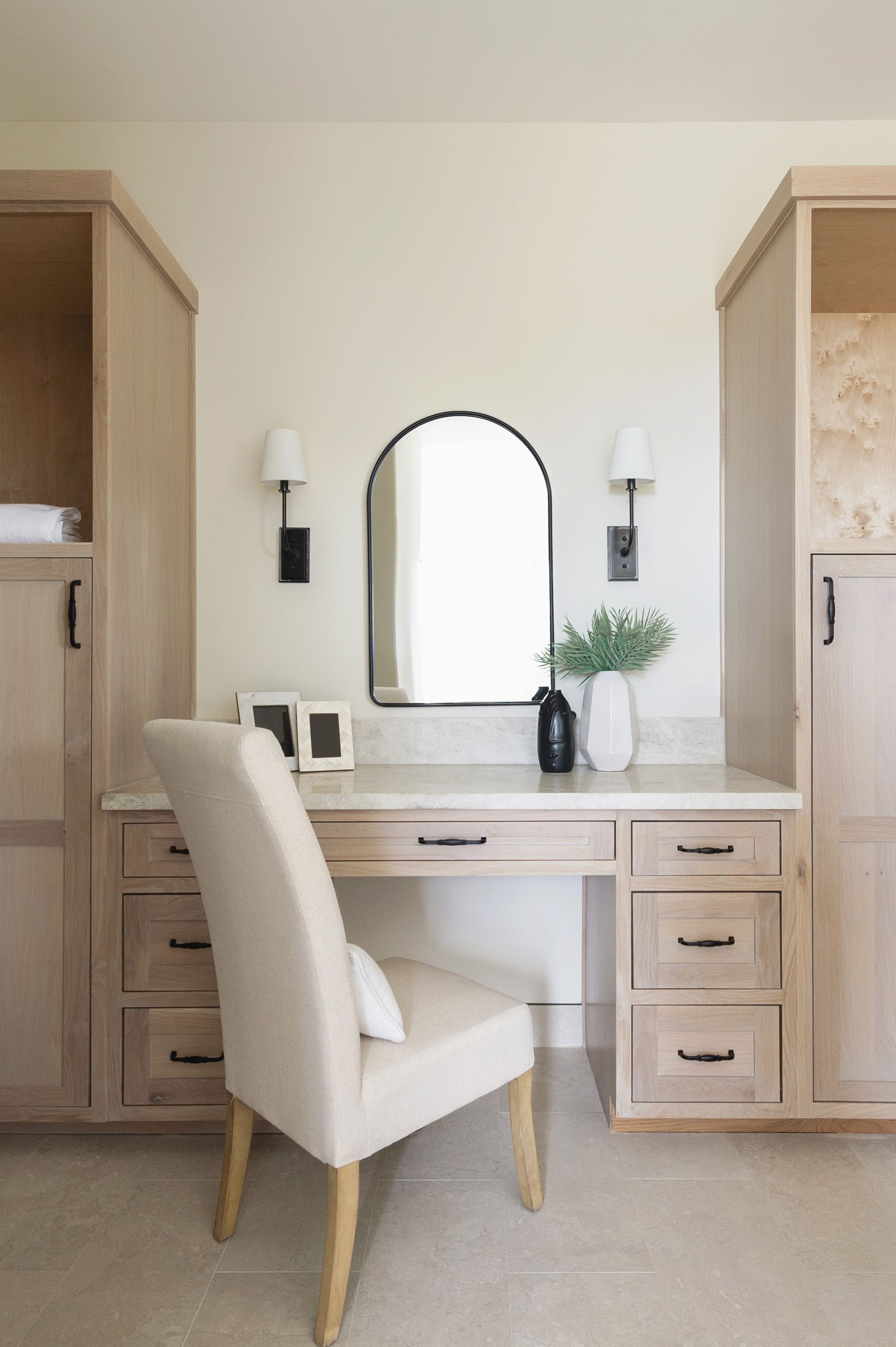 White vanity desk with mirror, chair, drawers, and wall sconces in a light-colored bedroom nook