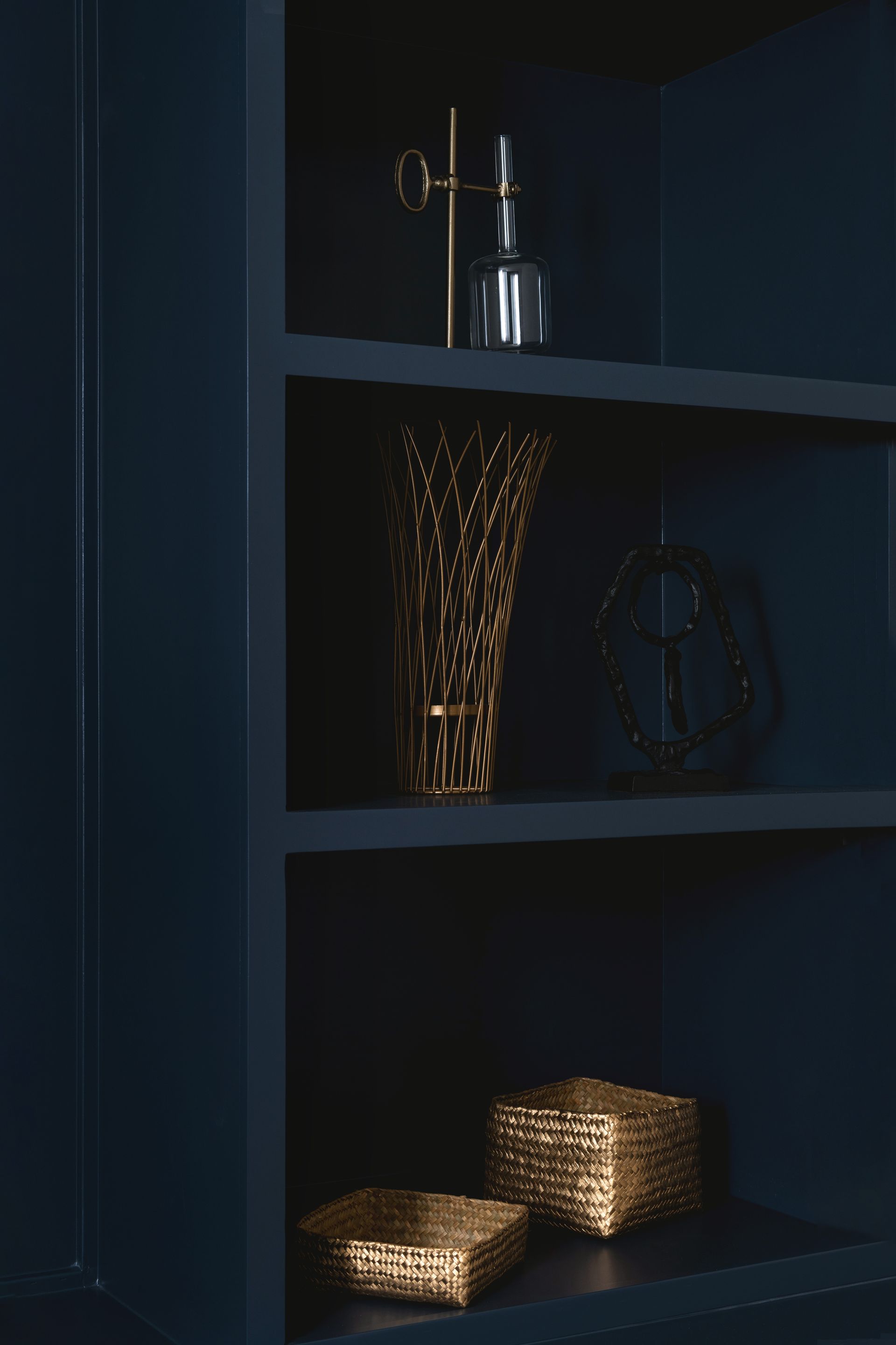 Dark shelf with glass decor and glowing woven baskets on a lower shelf