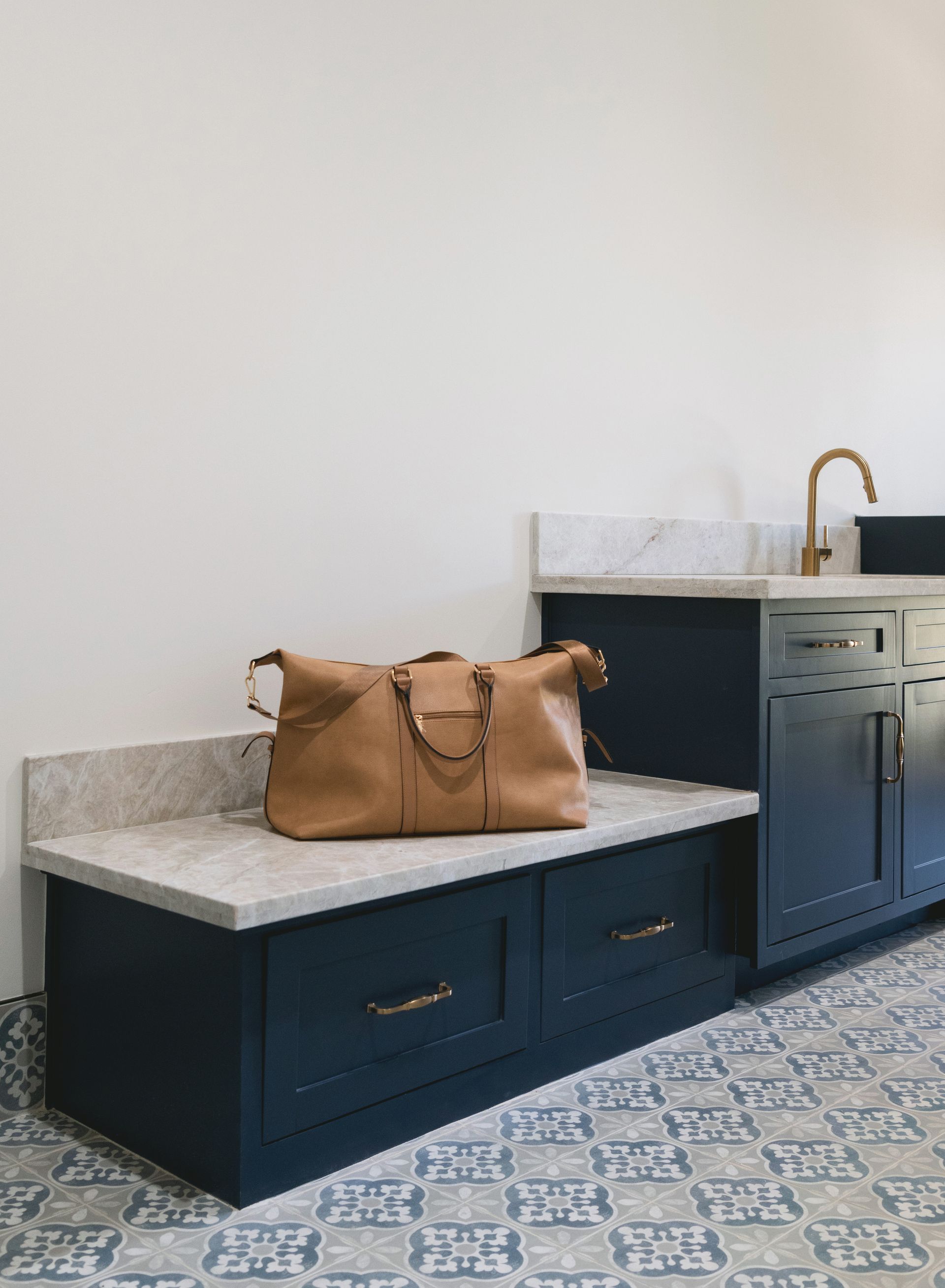 Tan kitchen island with marble top, tan handbag, dark blue cabinets, sink, and patterned tile floor.
