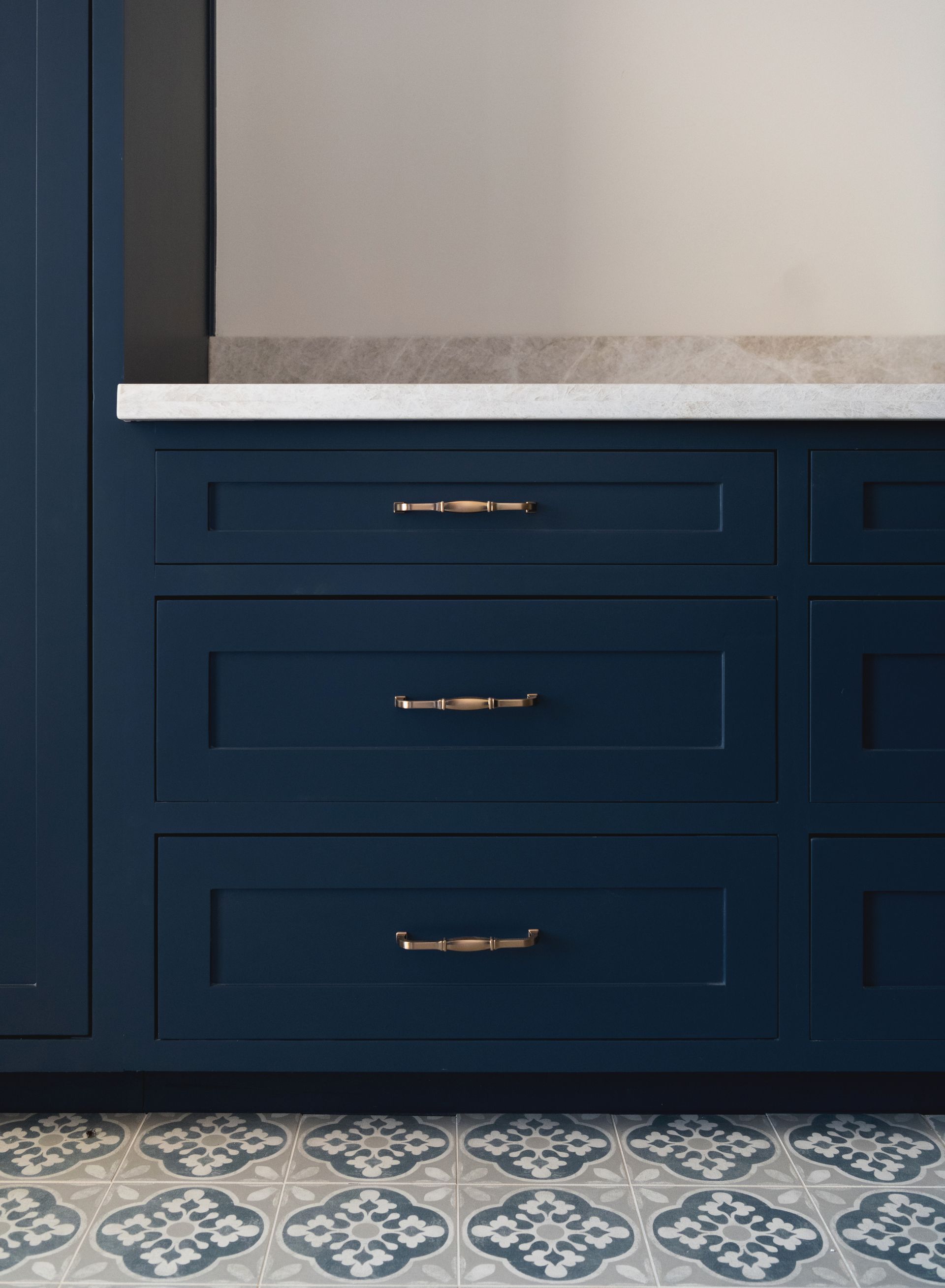 Navy blue bathroom vanity with brass pulls, white countertop, and patterned tile floor below