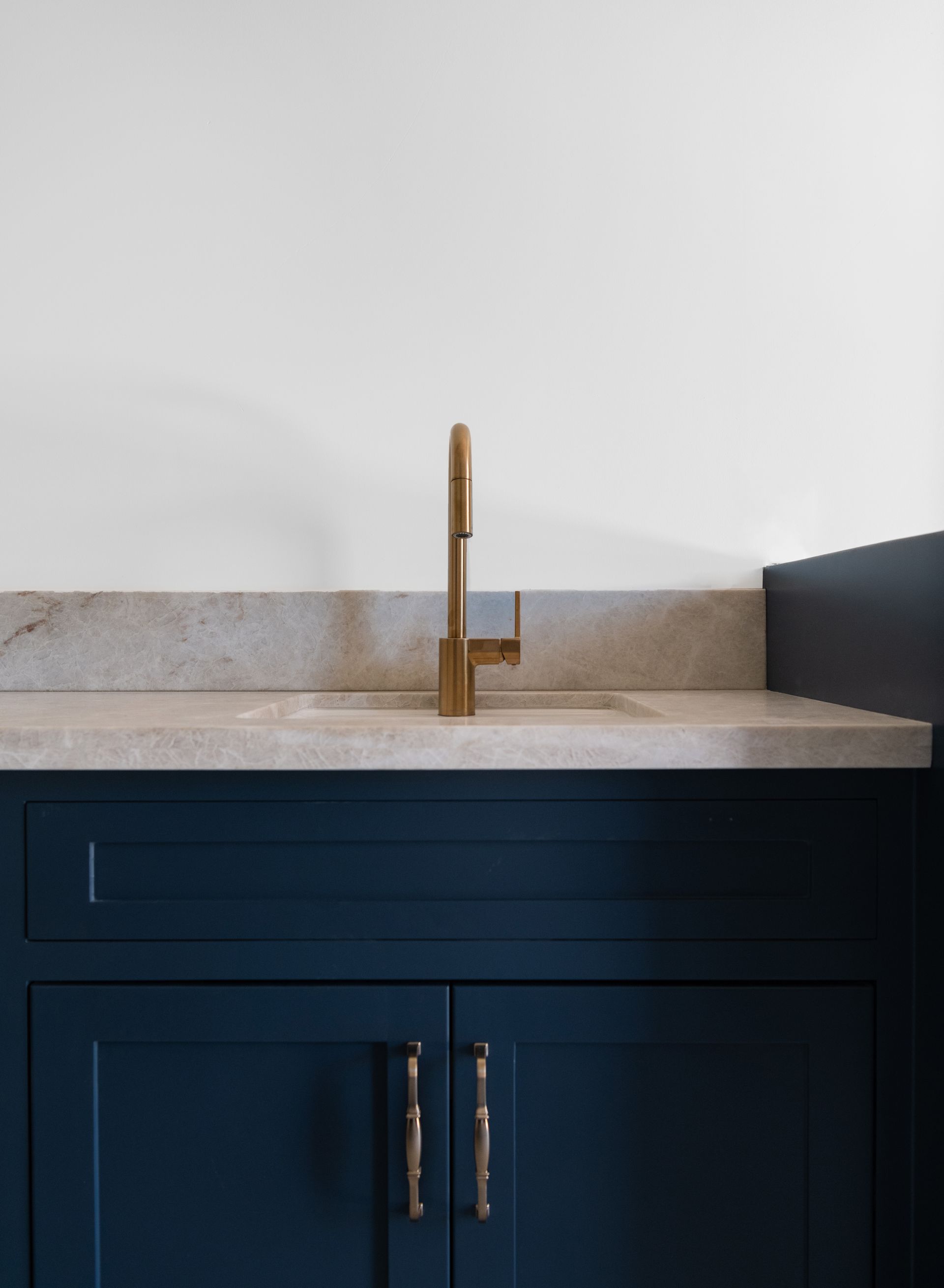 Dark blue bathroom vanity with brass faucet and white countertop against a light wall.