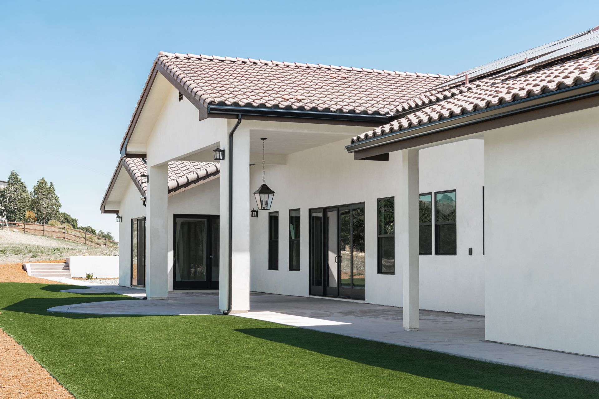 White stucco house with a tiled roof, covered patio, and green lawn on a sunny day