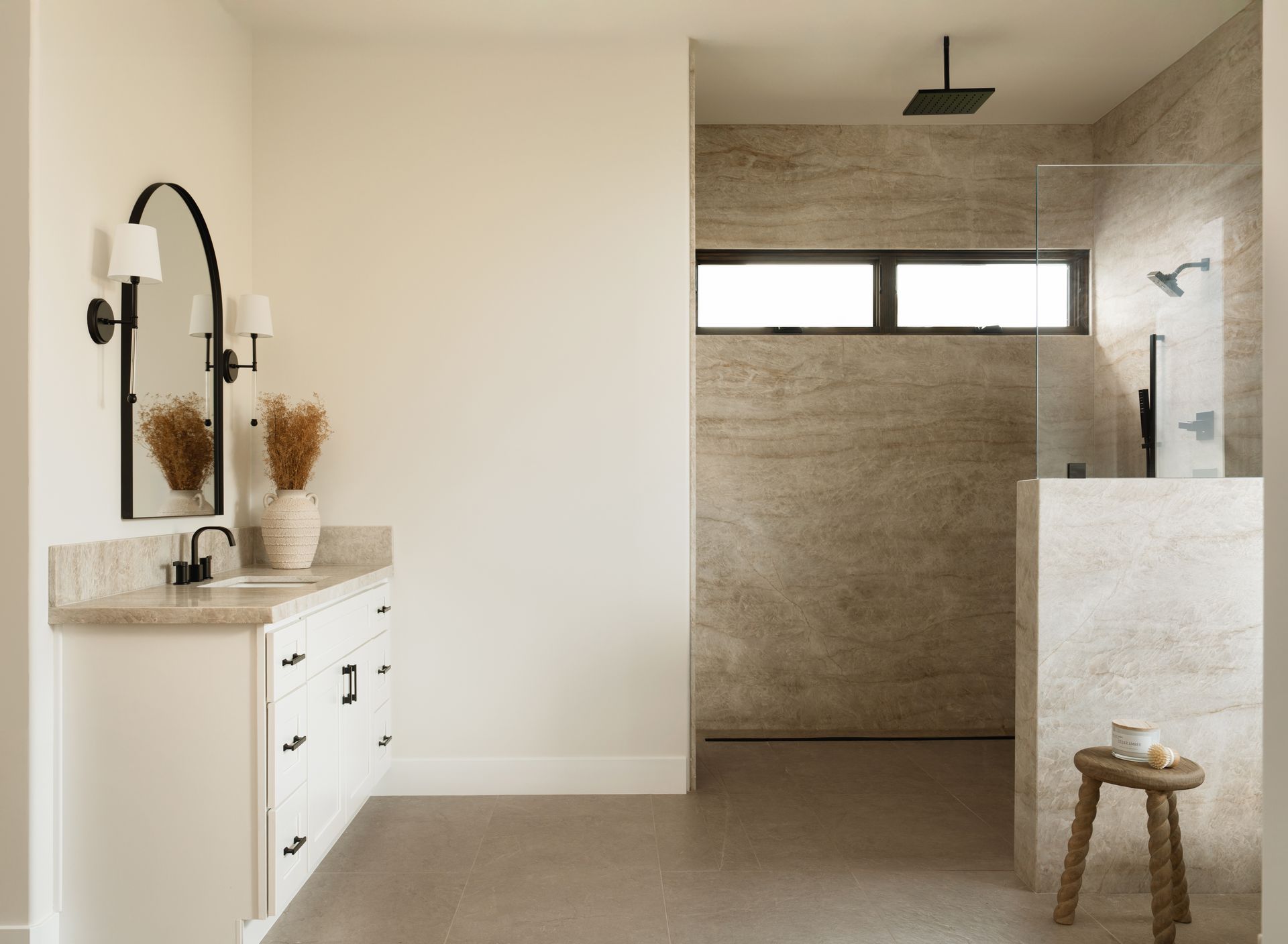 Modern bathroom with a vanity, walk-in shower, neutral tones, and a small stool by a stone counter.