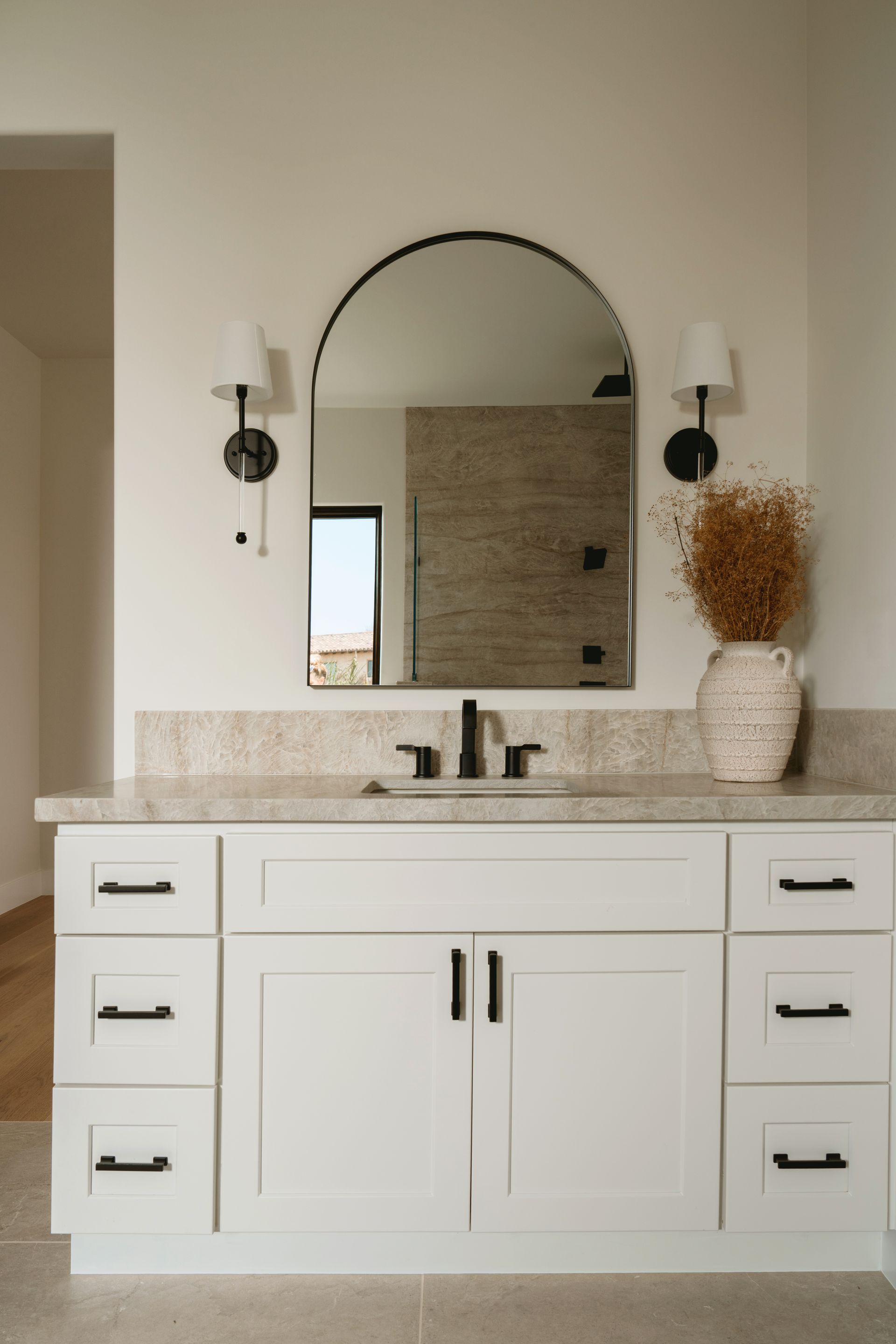 Modern bathroom vanity with arched mirror, wall sconces, and white cabinetry