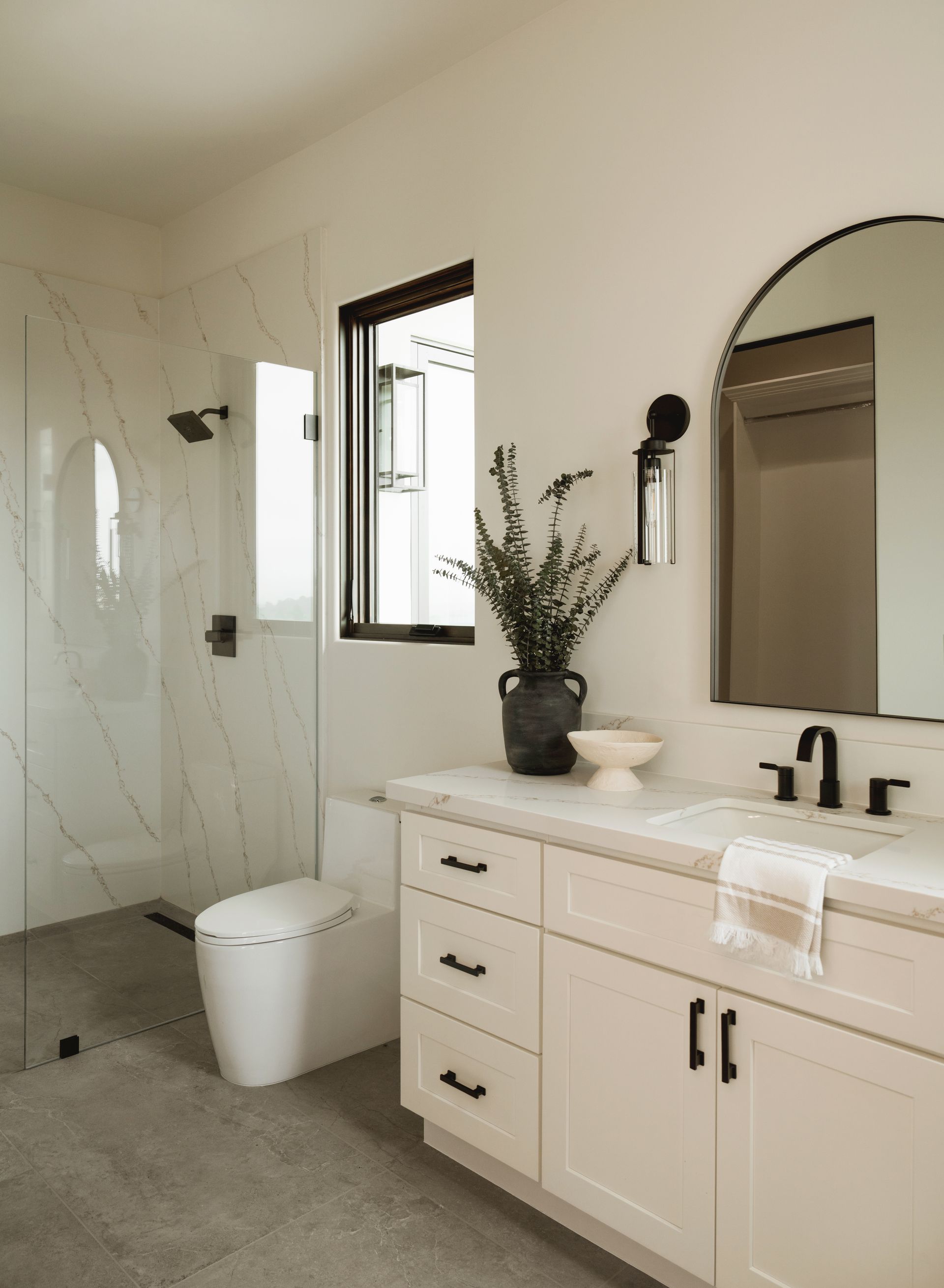 Modern bathroom with marble shower, white vanity, oval mirror, and a small plant on the counter