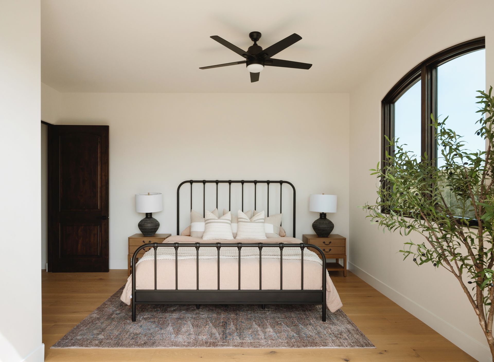 Minimal bedroom with black metal bed, white bedding, wood nightstands, and arched window.