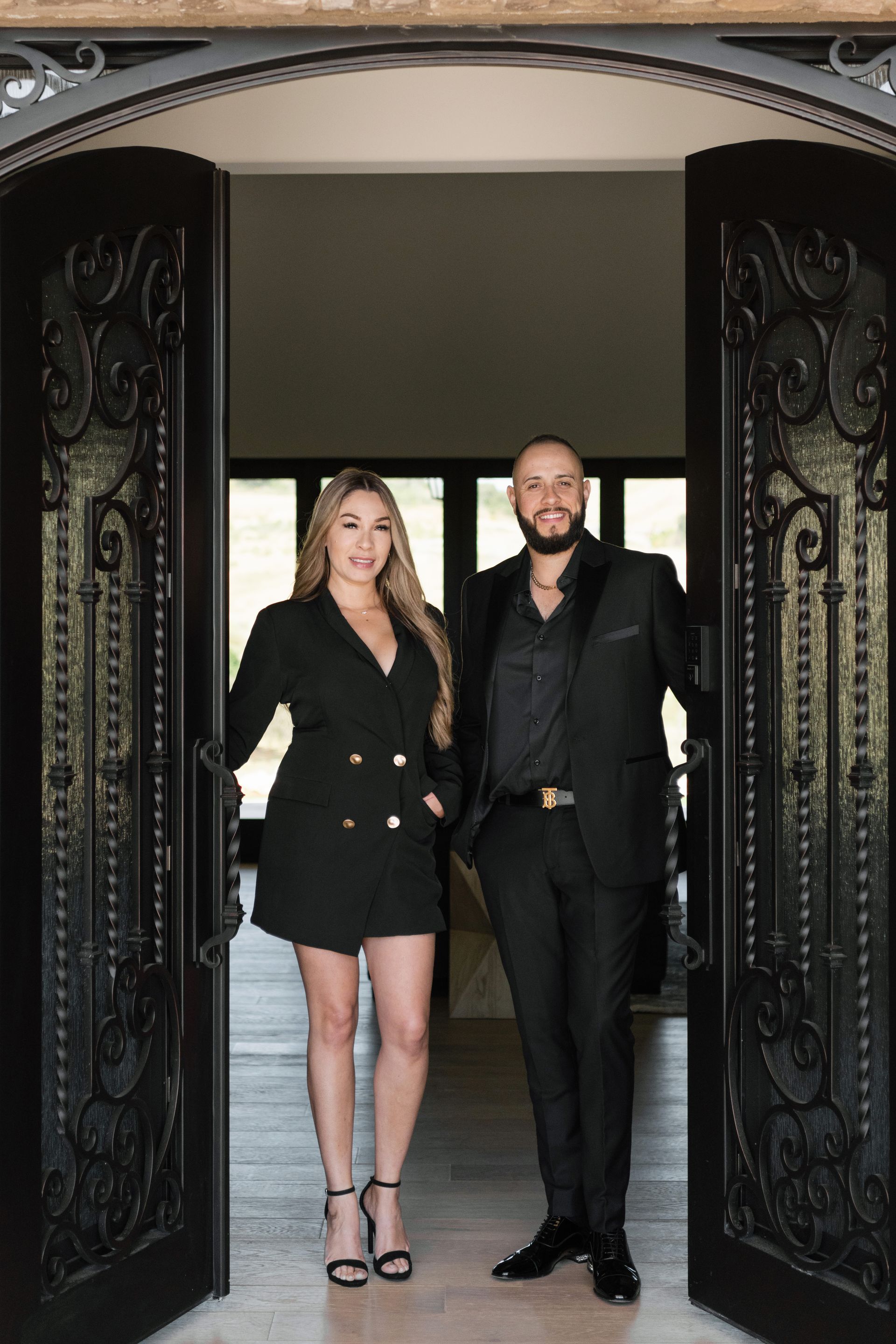 Two people posing in an ornate doorway, wearing black outfits.