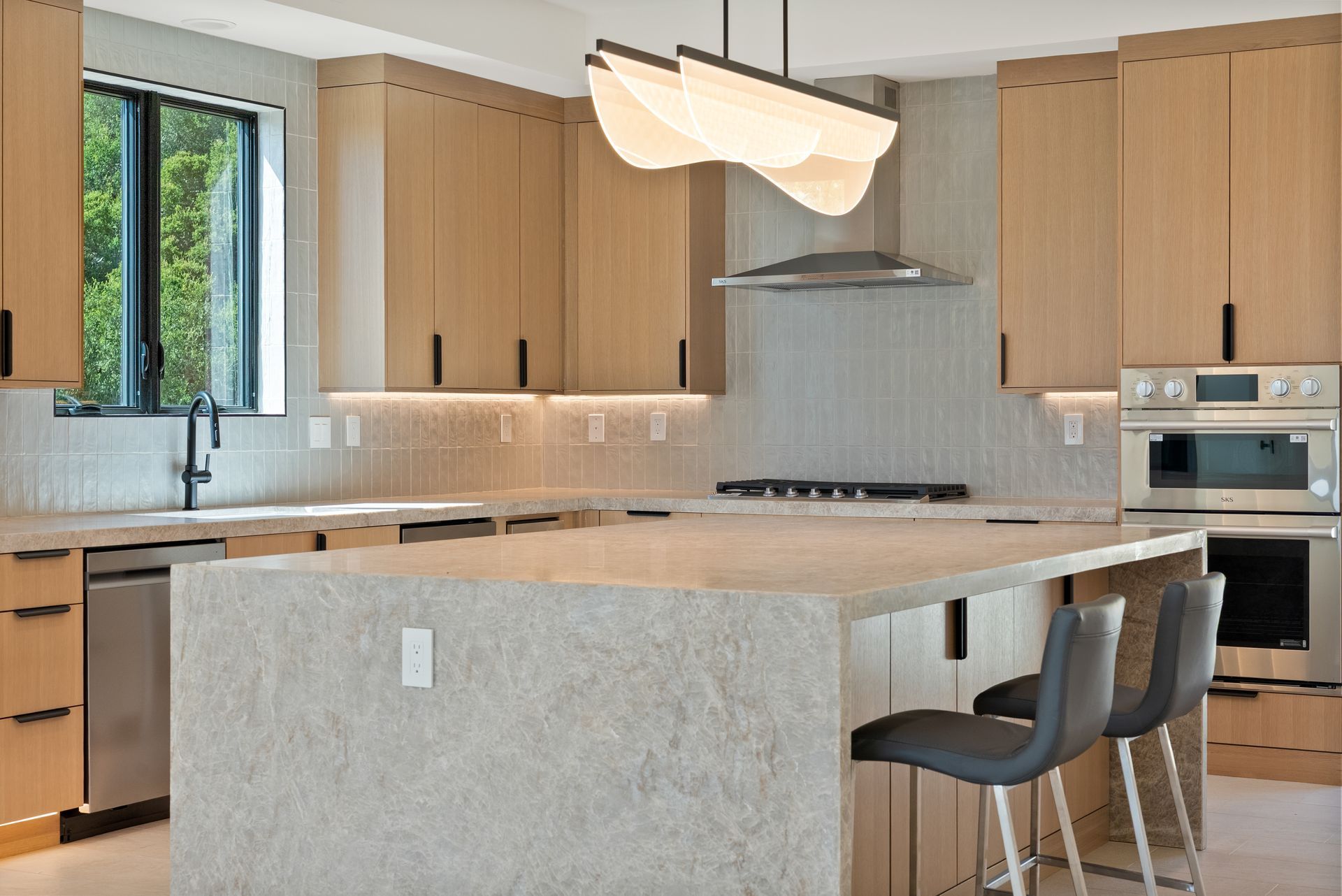 Modern kitchen with light wood cabinets, island seating, and stainless steel appliances