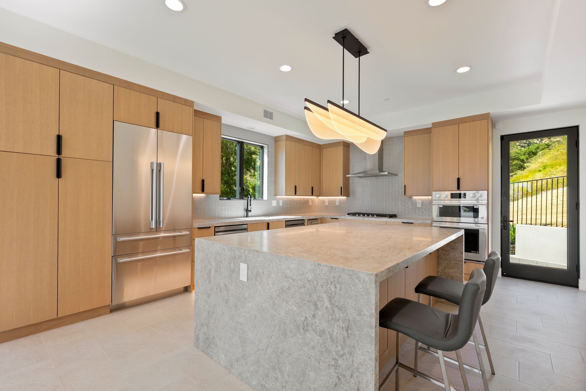 Modern kitchen with wood cabinets, stainless steel appliances, large island, and bar stools