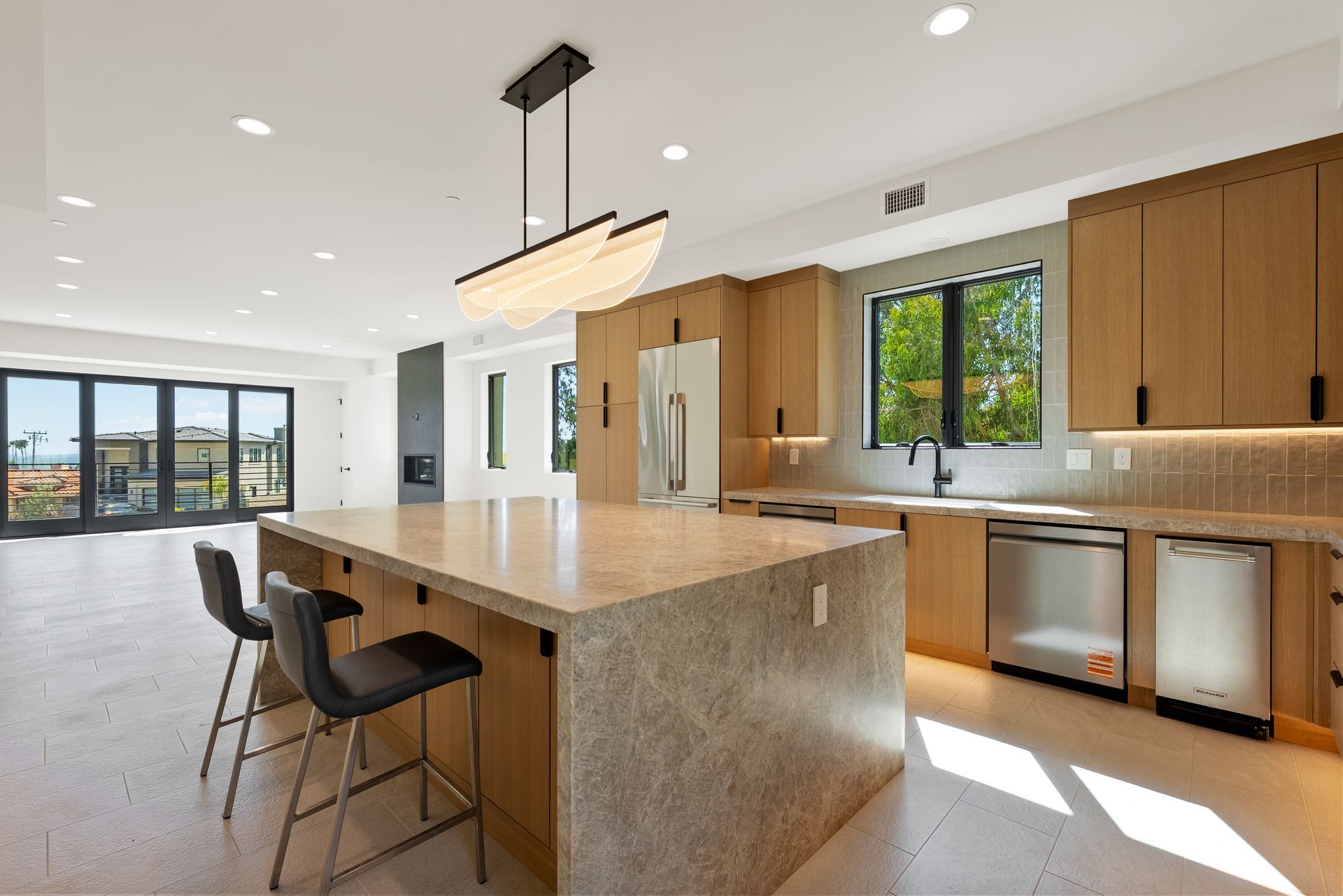 Modern kitchen with large island, wood cabinets, stainless appliances, and bright windows