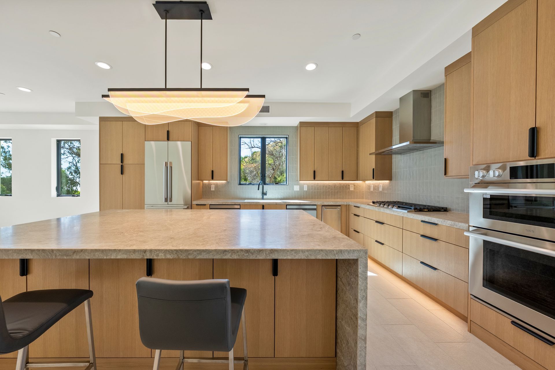 Modern kitchen with large island, wood cabinets, white counters, and stainless steel appliances