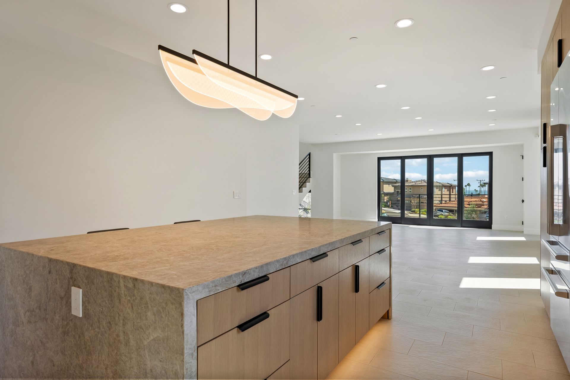 Modern open kitchen with large island, white walls, and sunlit windows opening to an outdoor view
