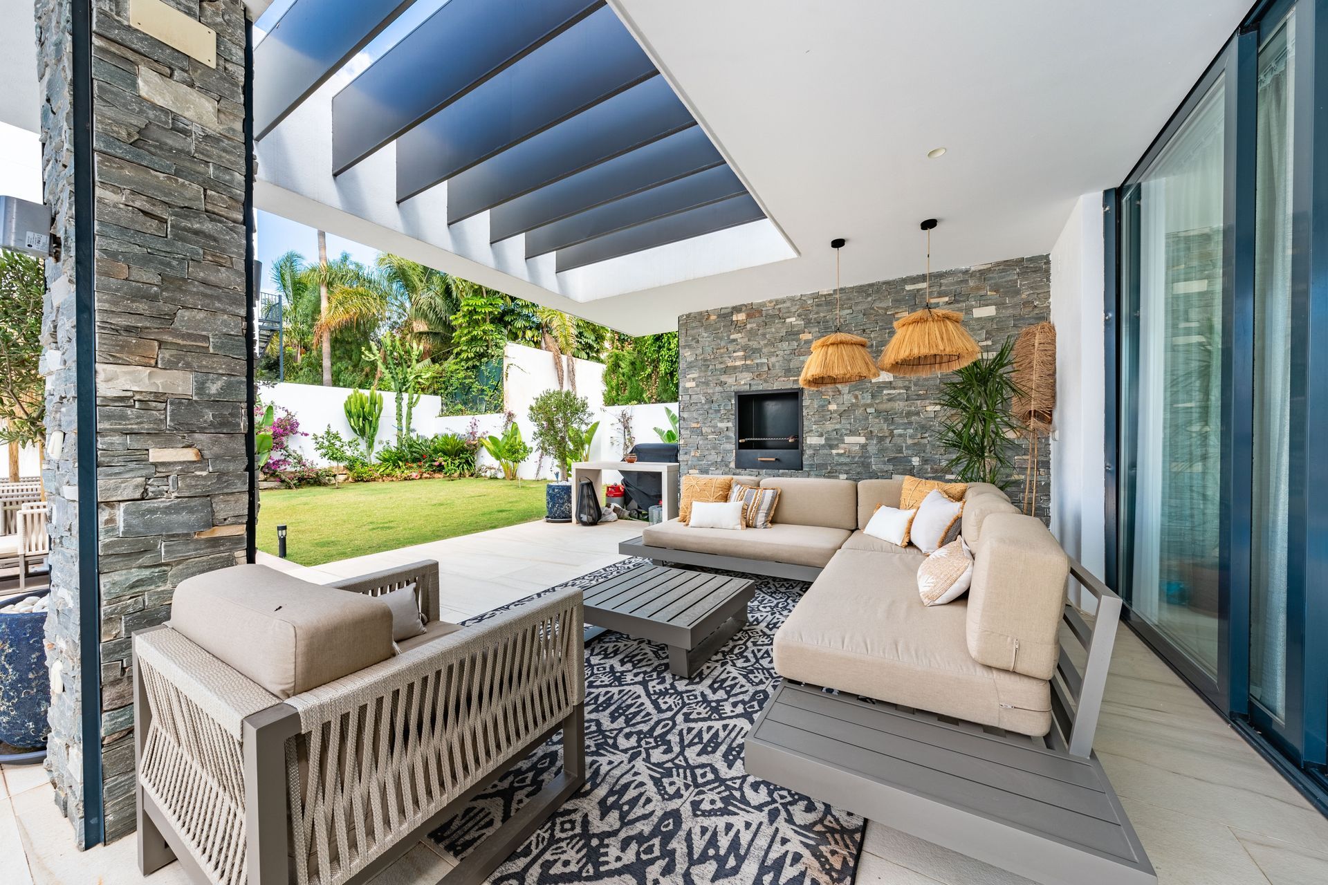 Modern covered patio with beige seating, patterned rug, stone fireplace, and sliding glass doors