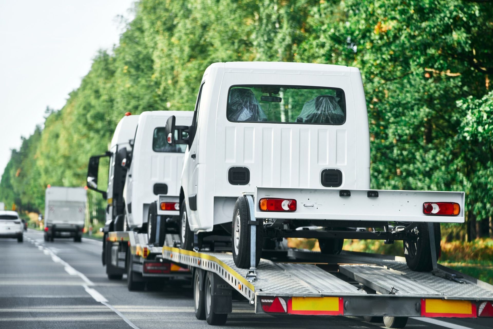A Tow Truck is Carrying a Row of White Vans Down a Highway — Hervey Bay Tilt Tray Hire In Maryborough, QLD