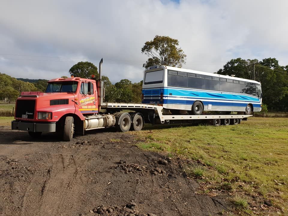 A Red Semi Truck is Towing a Blue and White Bus on a Flatbed Trailer — Hervey Bay Tilt Tray Hire In Bundaberg, QLD