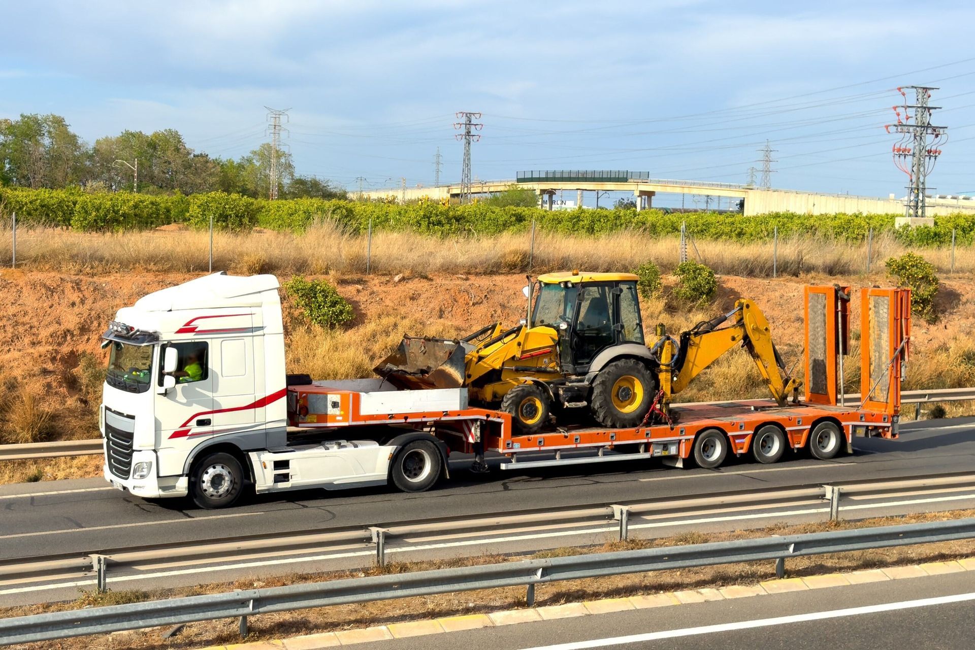A Semi Truck is Carrying a Tractor on a Trailer on a Highway — Hervey Bay Tilt Tray Hire In Childers, QLD