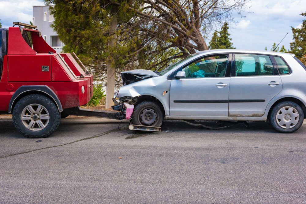 A Tow Truck is Towing a Damaged Car on the Side of the Road — Hervey Bay Tilt Tray Hire In Maryborough, QLD