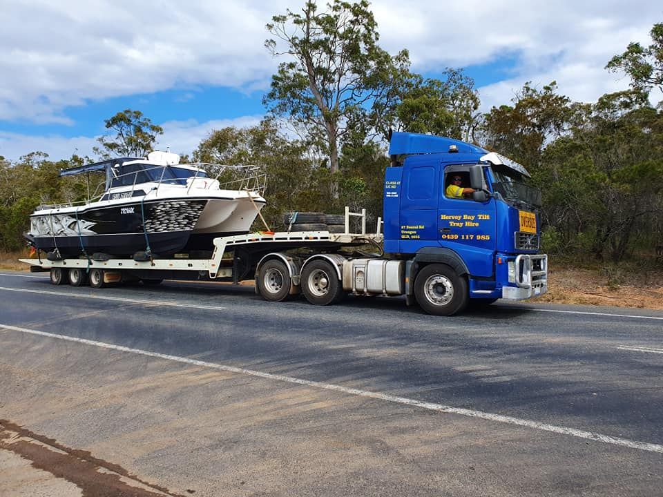 A Blue Semi Truck is Carrying a Boat Down a Road — Hervey Bay Tilt Tray Hire In Bundaberg, QLD