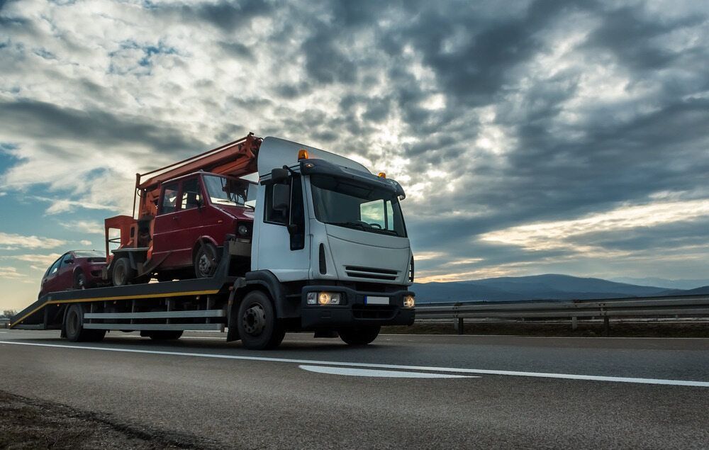 A Tow Truck is Driving Down a Highway Carrying a Red Car — Hervey Bay Tilt Tray Hire In Childers, QLD