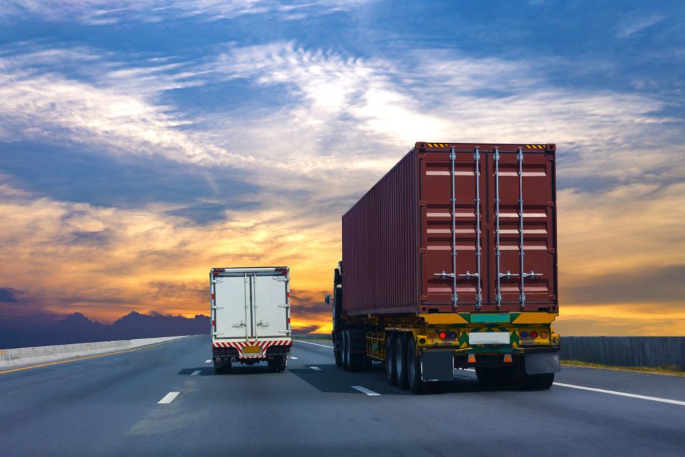 Two Semi Trucks Are Driving Down a Highway at Sunset — Hervey Bay Tilt Tray Hire In Maryborough, QLD
