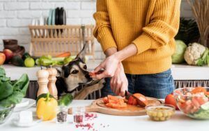 A woman is cutting vegetables in a kitchen with her dog.