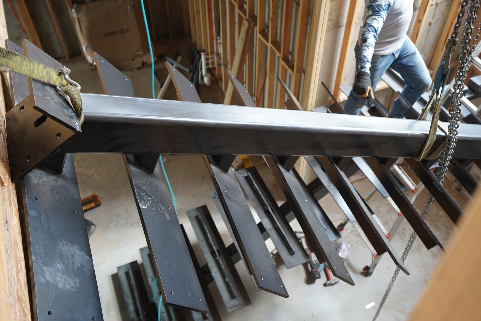 Indoor construction site with workers installing a steel beam and staircase frame.
