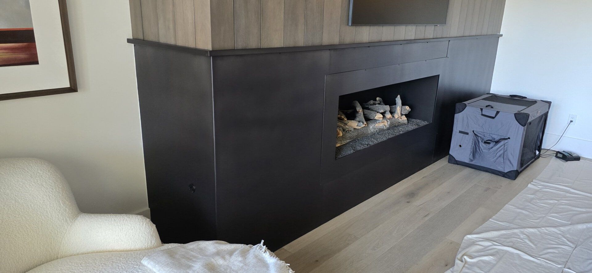 Modern bedroom with a black fireplace, light wood flooring, a chair, and a suitcase near the wall